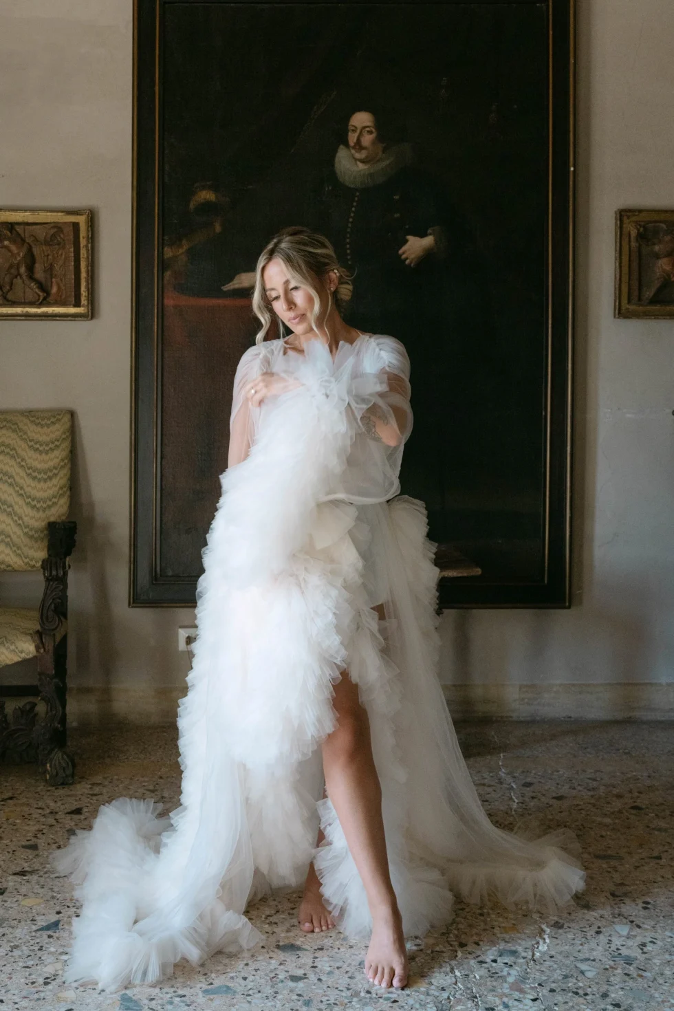 Beatrice in a feathered robe before a dark portrait painting at Castello Odescalchi