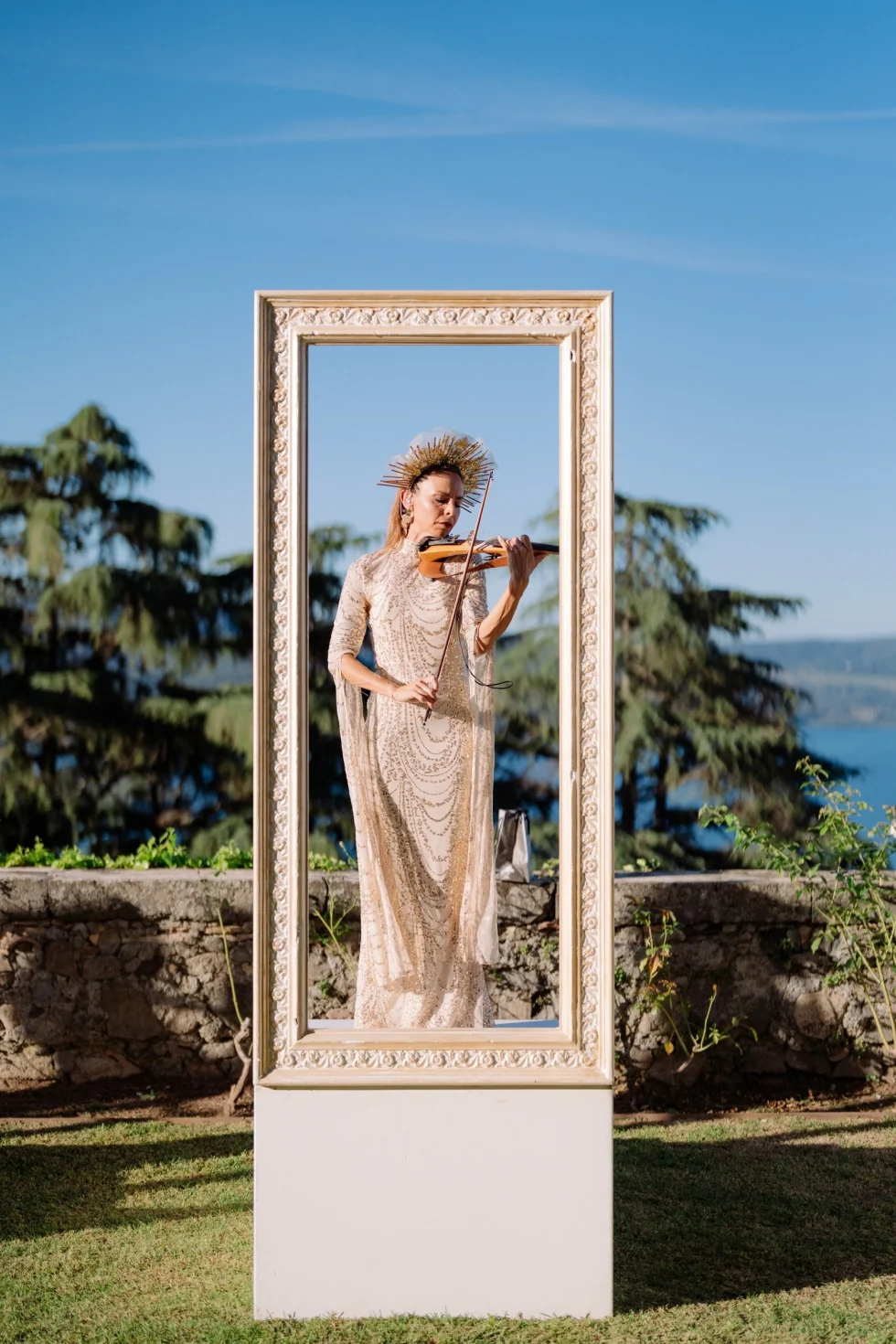 A violinist in a golden crown playing inside a carved frame above Lake Bracciano at Castello Odescalchi