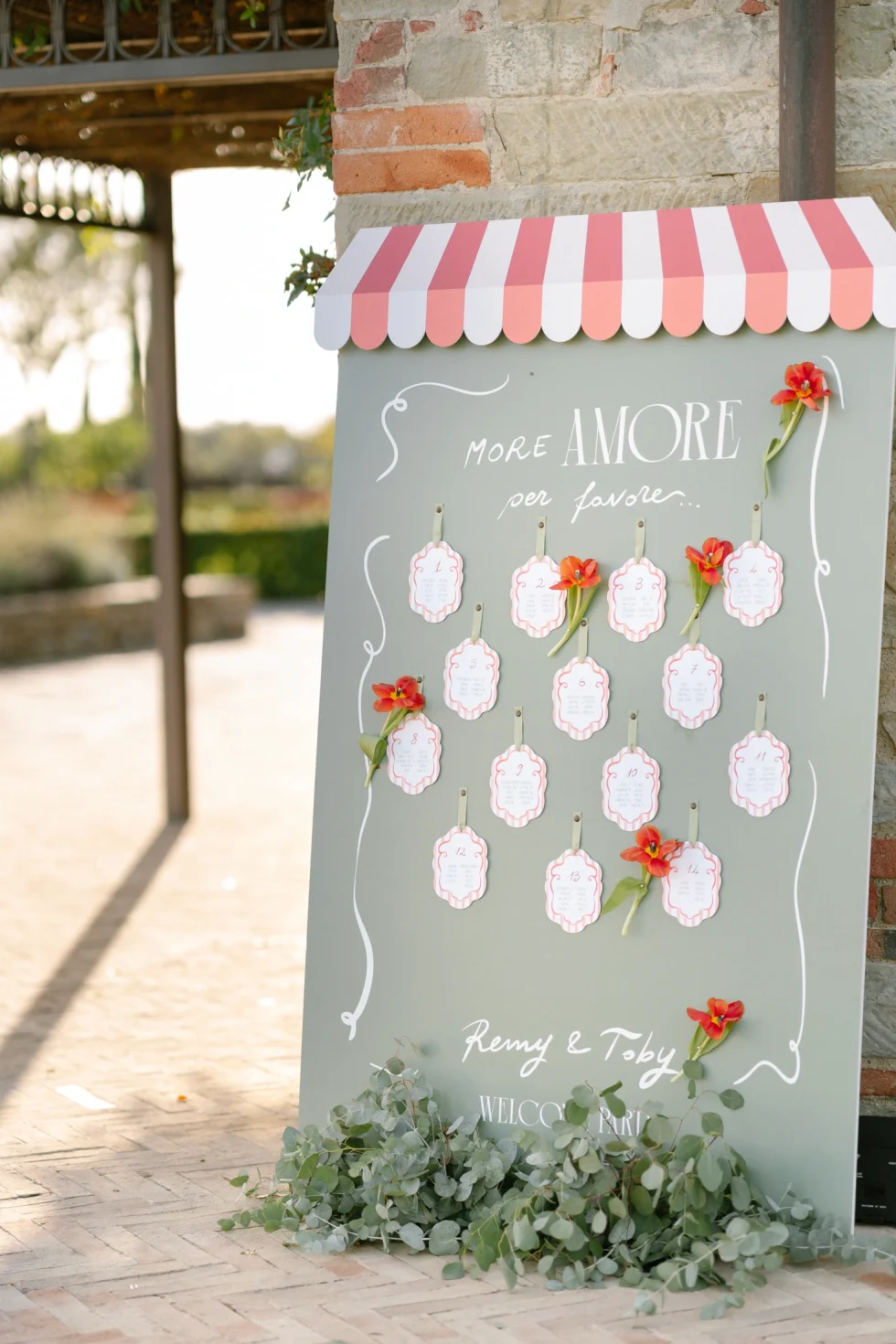 A welcome sign with a striped awning and red flowers for Remy and Toby's pizza party at Il Borro