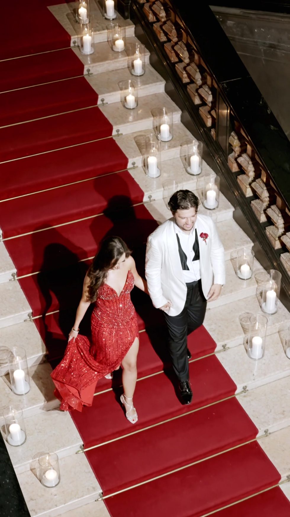 Renee in a red evening gown and Tino descending the candlelit red staircase of Villa Erba