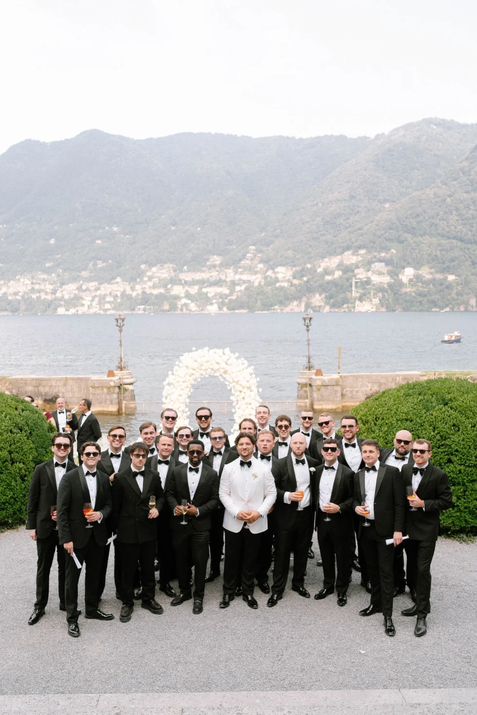 Groom and groomsmen in black tie by the floral arch on Lake Como, Villa Erba