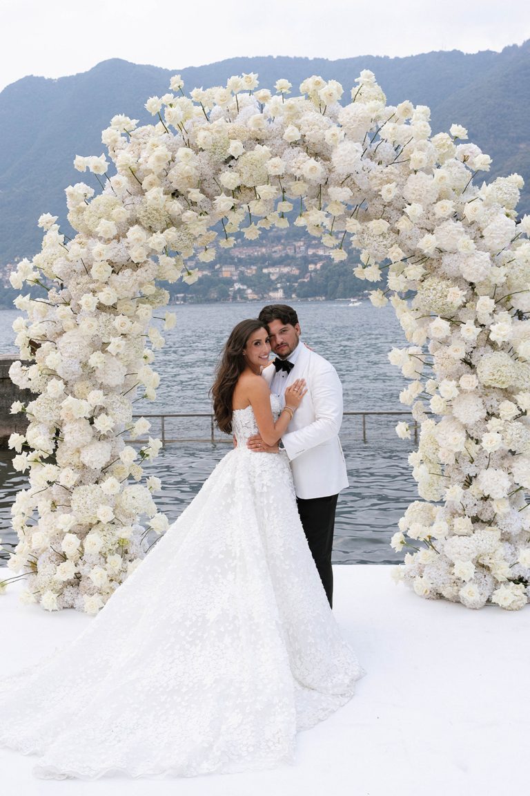 Couple embracing under a white rose arch over Lake Como, Villa Erba wedding