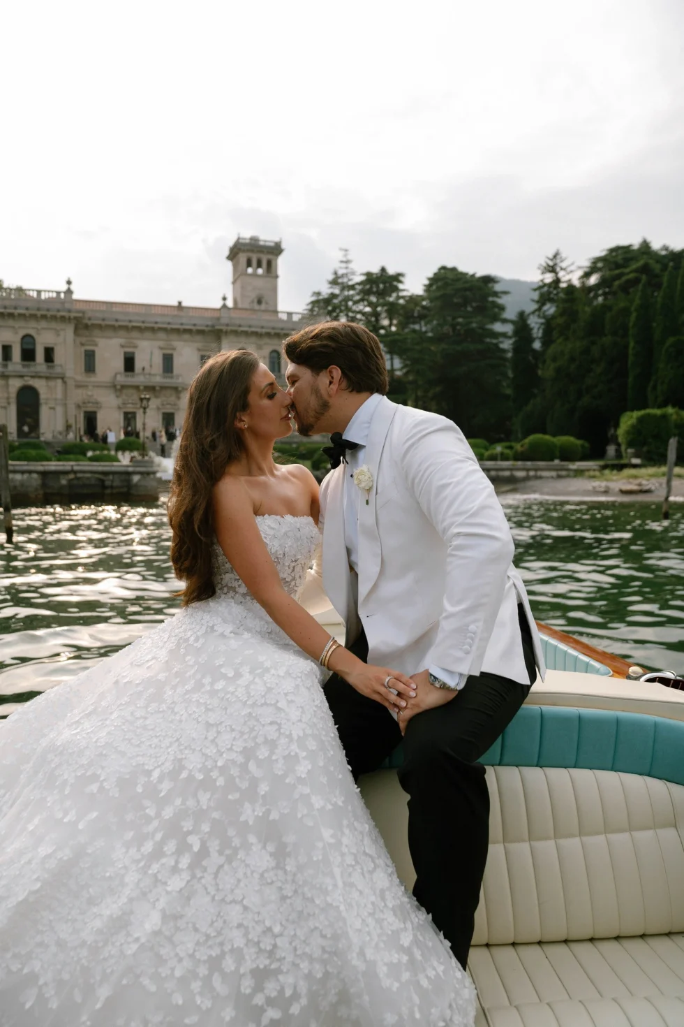 Renee and Tino kissing on a classic wooden boat in front of Villa Erba, Lake Como