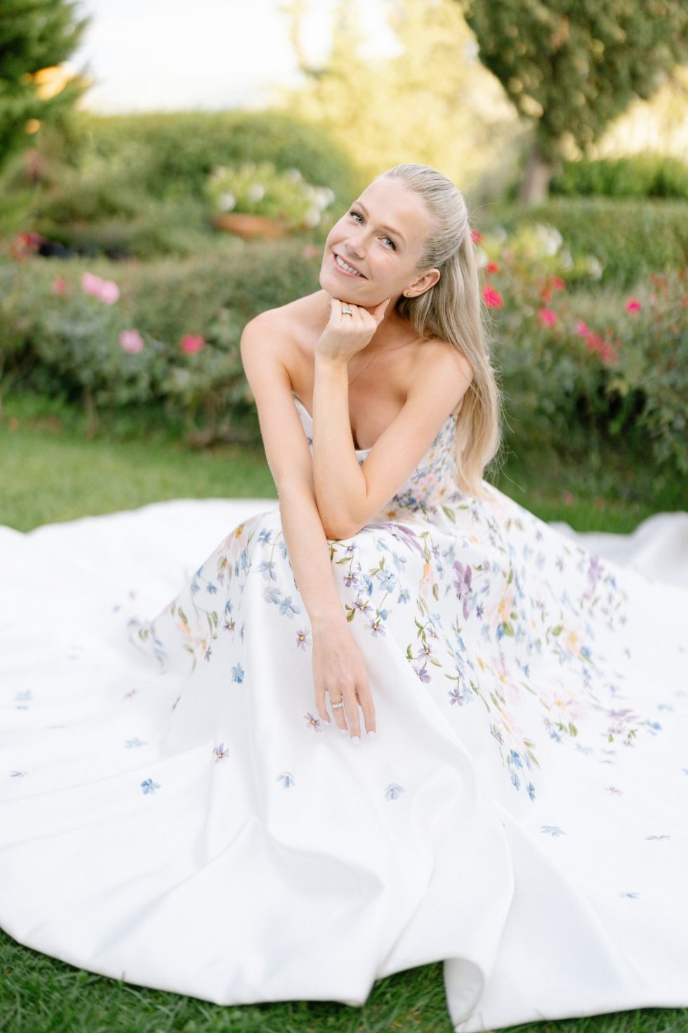 The bride crouching on the lawn in her floral gown among the roses at Borgo Vescine, near Siena