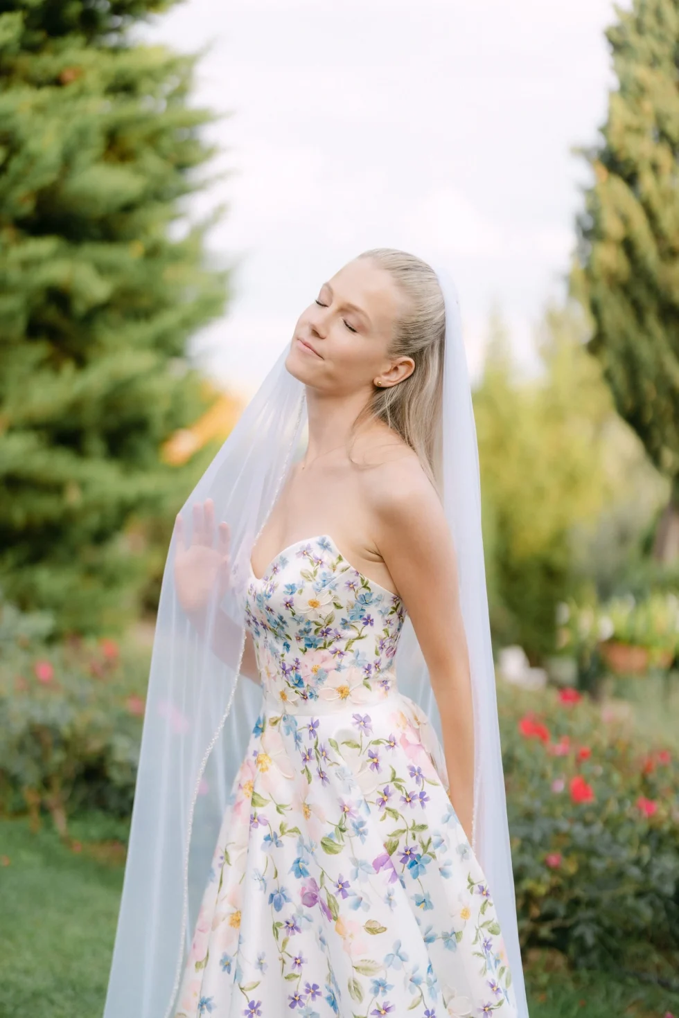 The bride in a floral gown and long veil among the cypresses at Borgo Vescine, near Siena