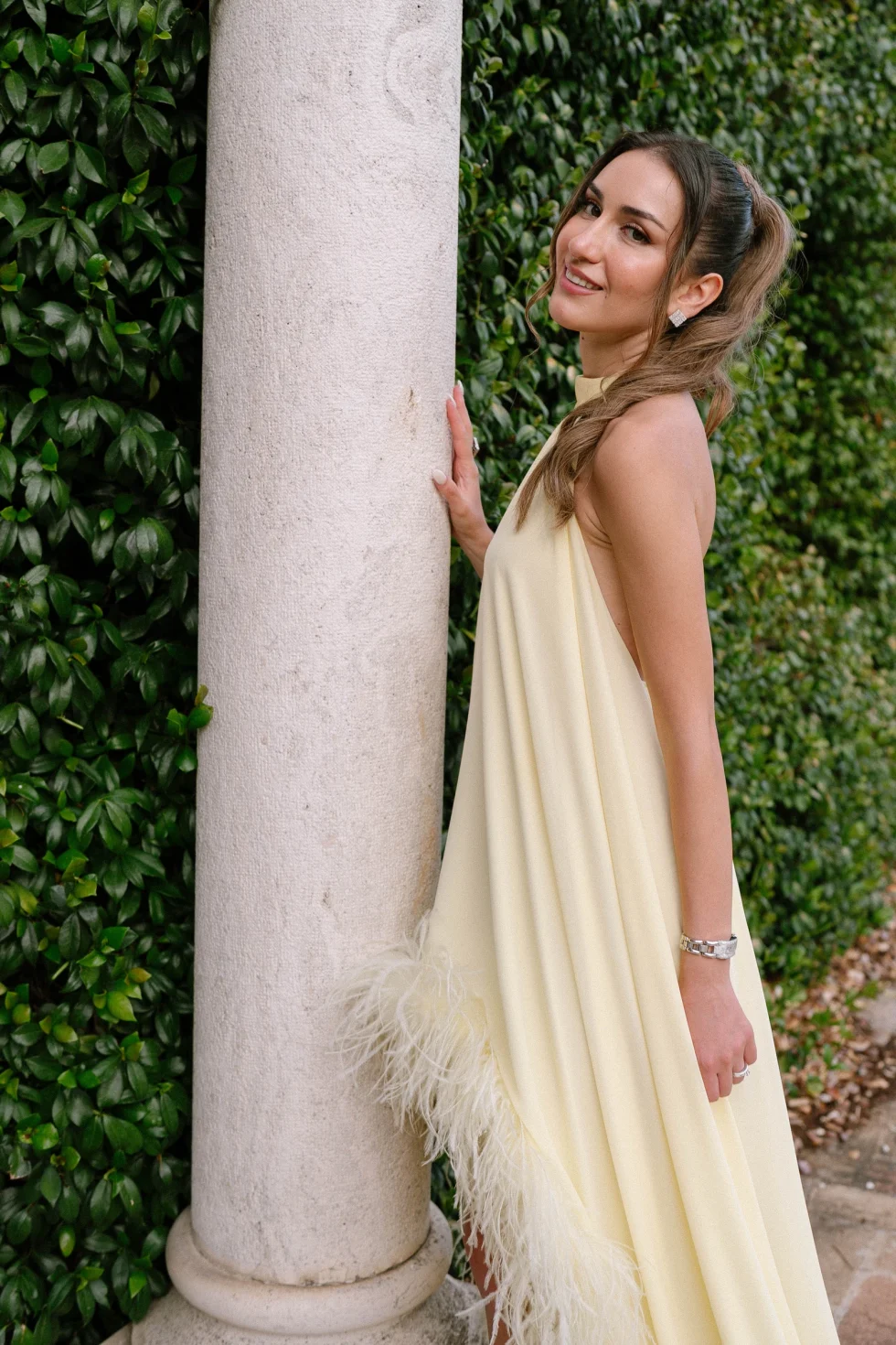 Suzanne in a pale yellow feathered gown beside an ivy-covered column at Palazzo di Bagnaia, Umbria