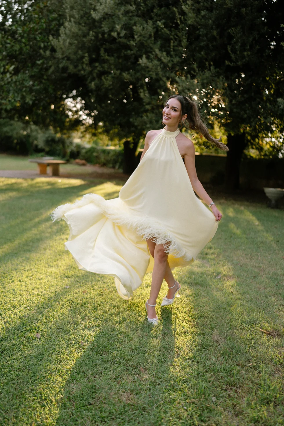 Wedding photographer in Umbria: Suzanne twirling her feather-trimmed gown in the late sun, in the park of Palazzo di Bagnaia